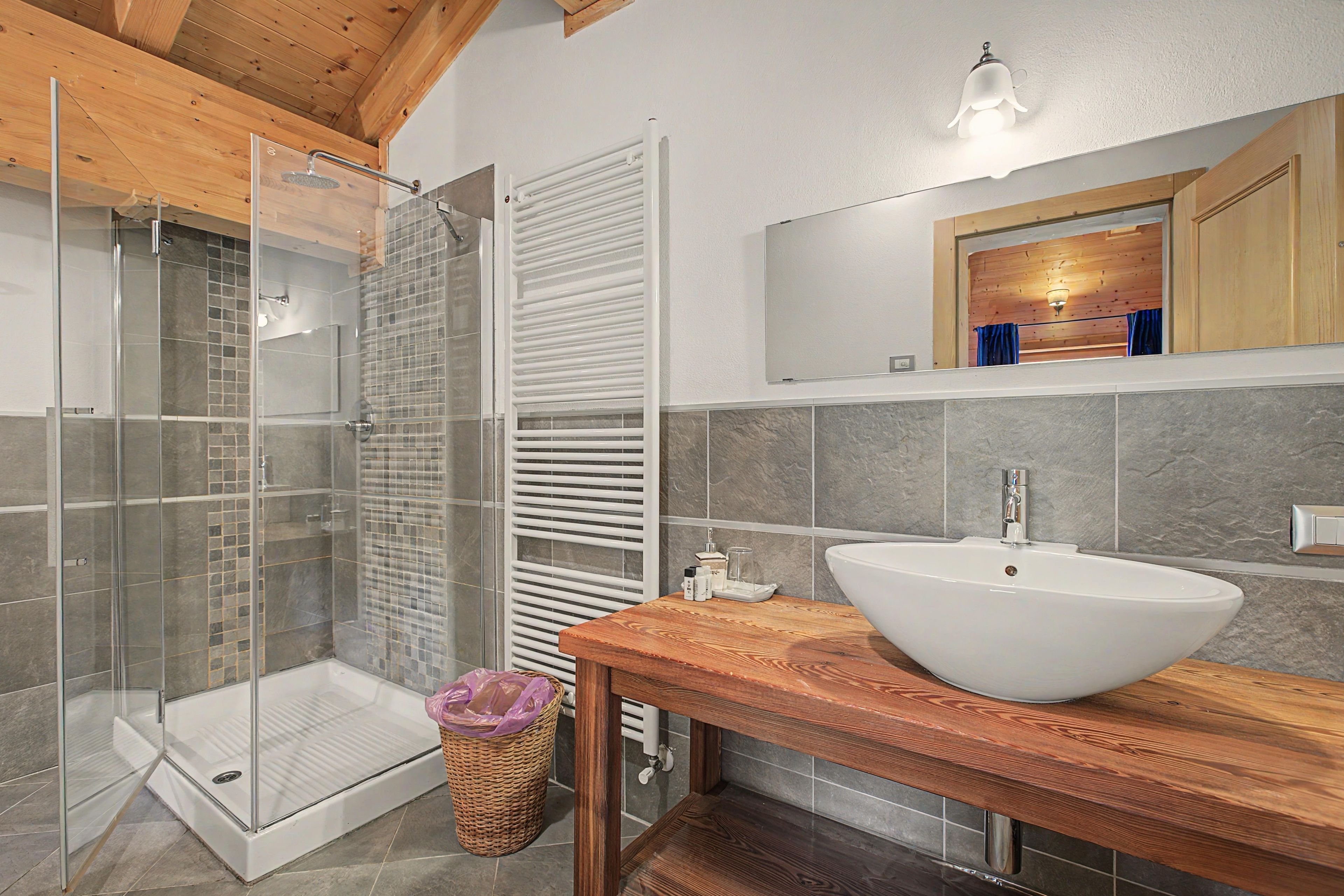 Une salle de bain moderne avec une douche à parois de verre, un meuble-lavabo en bois doté d’un grand évier et un porte-serviettes.