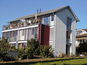 Een gebouw met twee verdiepingen, een balkon, grote ramen en een rode accentmuur.