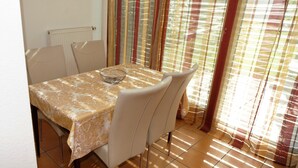 Een eethoek met een tafel, bedekt met een tafelkleed met een patroon, vier stoelen, een kom en een radiator.