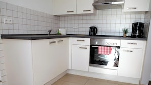 Una cocina con gabinetes blancos, encimera negra, horno de acero inoxidable y cafetera.