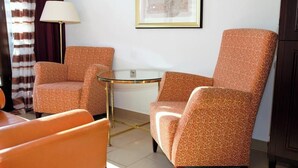 Una habitación con dos sillones estampados, una mesita redonda pequeña, una lámpara y un cuadro en la pared.