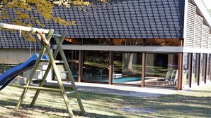 Un parque infantil con tobogán y escalera, una piscina y un edificio con grandes ventanales.