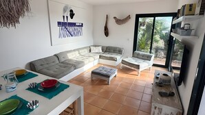 Un salon comprenant un canapé, un pouf et une table à manger mise avec des assiettes et un pichet.