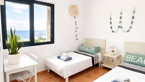 Une chambre avec deux lits, un bureau, une plante en pot et une vue sur la mer.