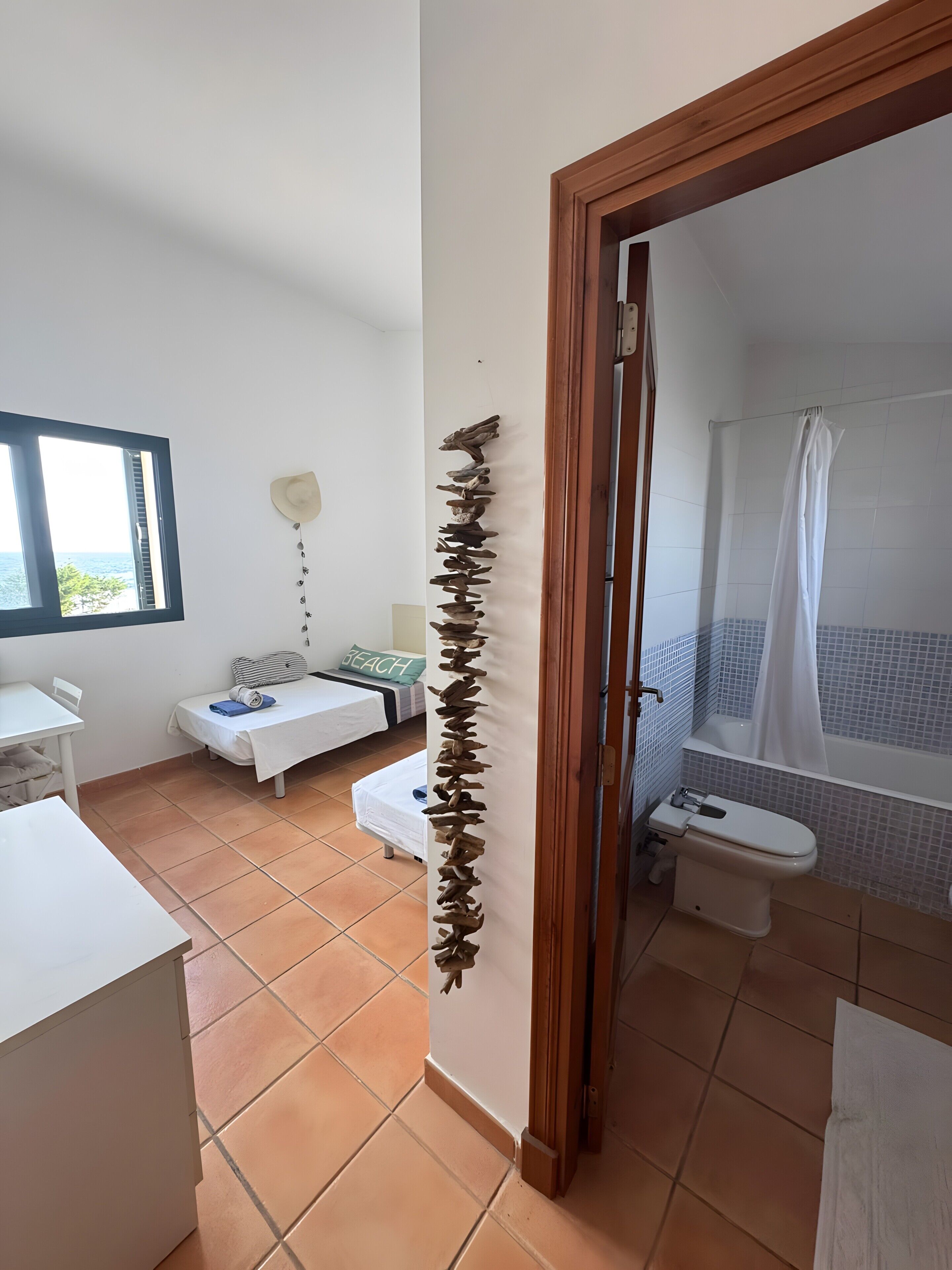 Una habitación con cama, escritorio, ventana con vistas, baño con bañera e inodoro, y un adorno en la pared.