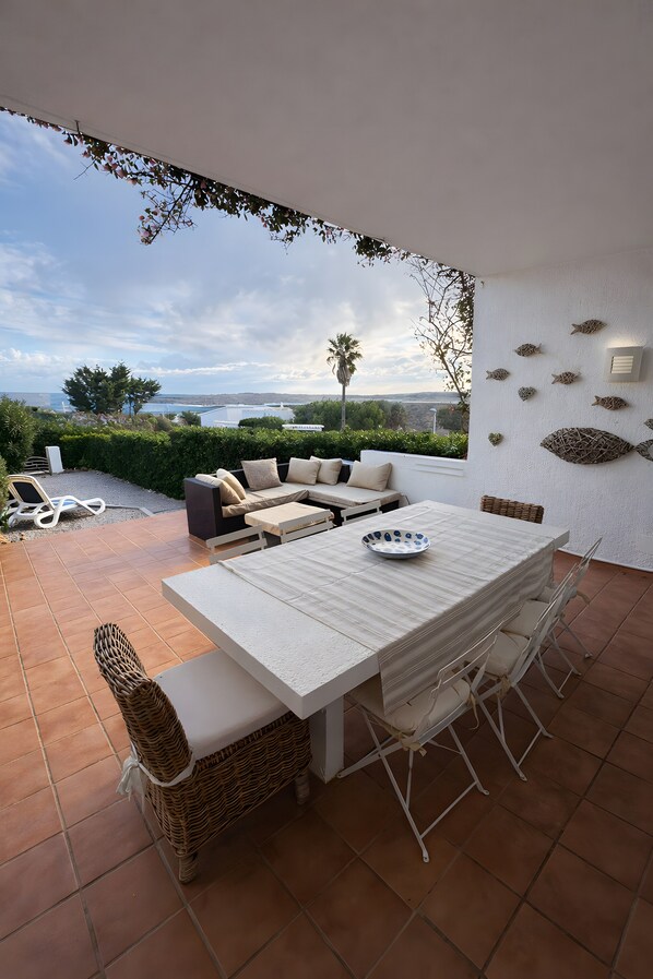 Eine Terrasse mit Tisch, Stühlen und einer Sitzecke, mit Blick auf das Meer.