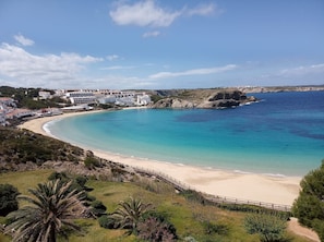Ein Küstenresort mit Sandstrand, einem Felsen und einem großen Gebäudekomplex.