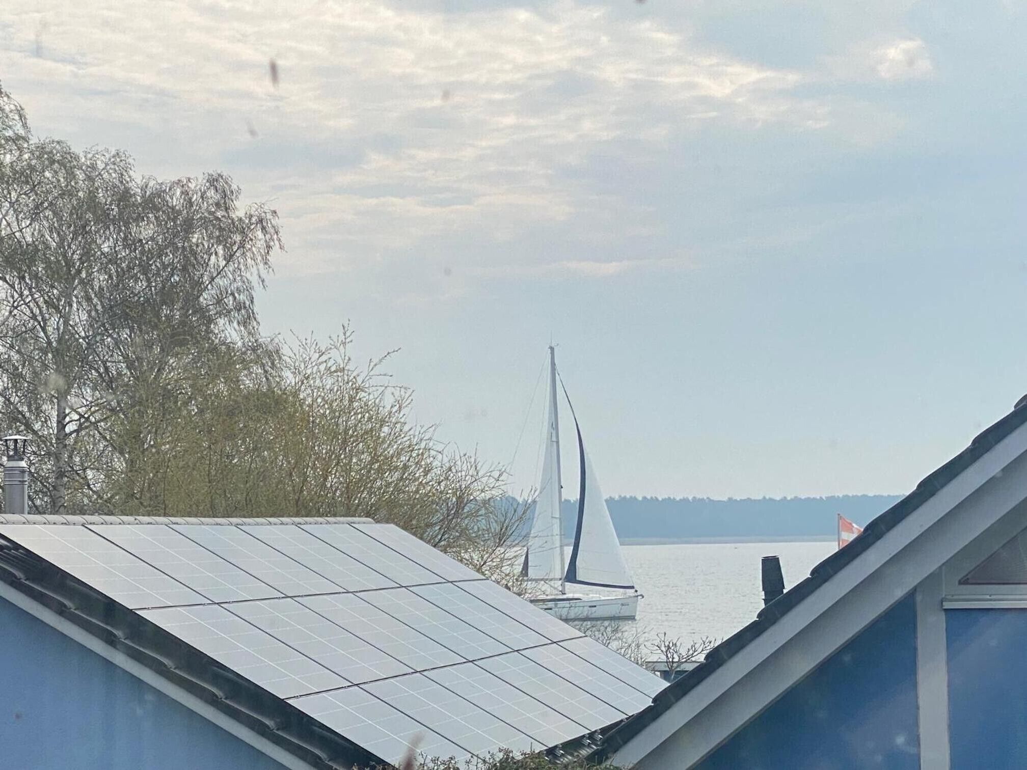 A building with a sloped roof, solar panels, and a sailboat on the water in the background.