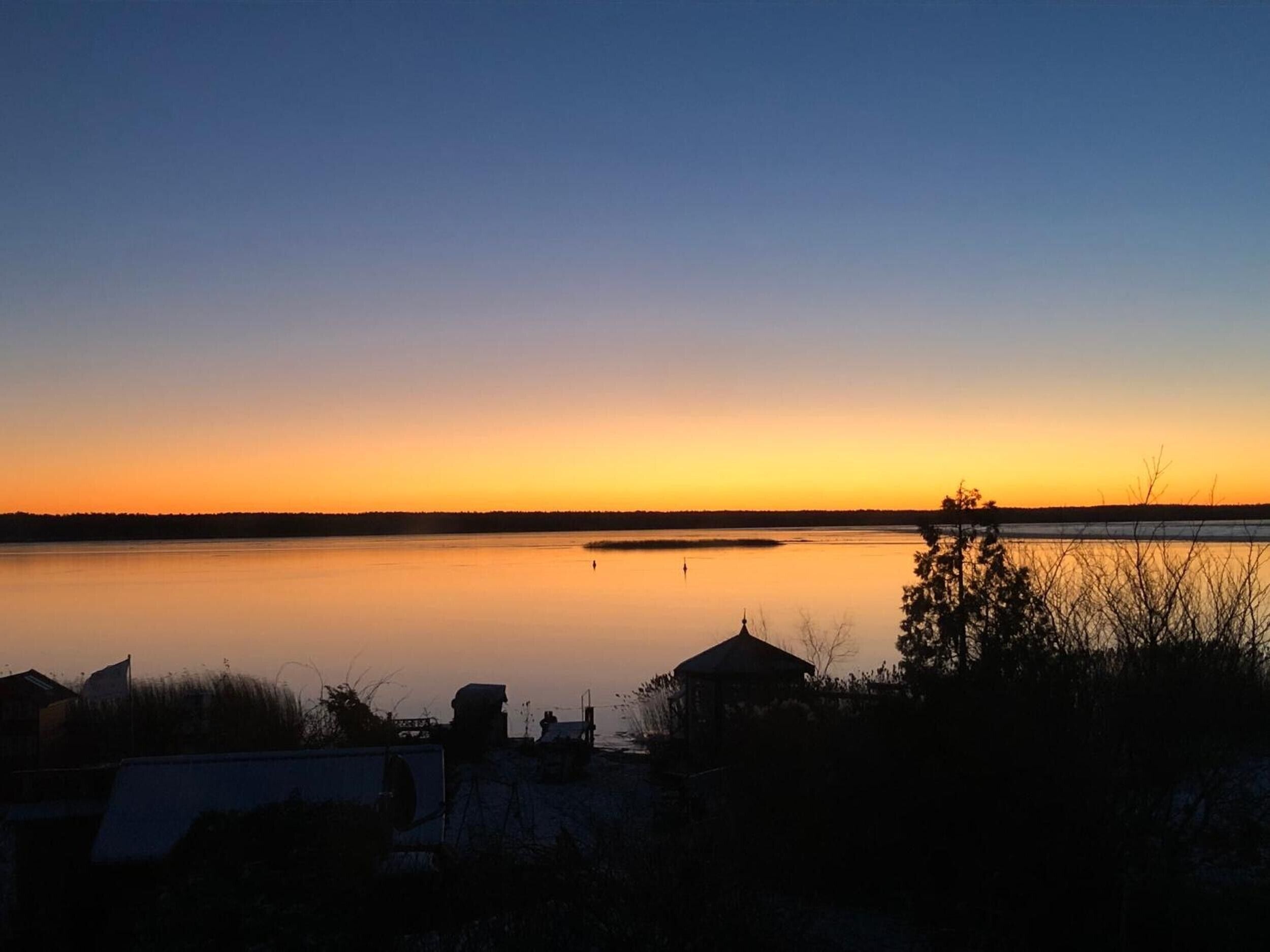 Un lac paisible au coucher du soleil, avec un petit bâtiment en premier plan.