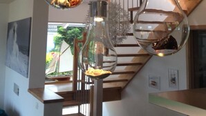 Un intérieur moderne avec un escalier, des luminaires suspendus et une vue sur l’extérieur.
