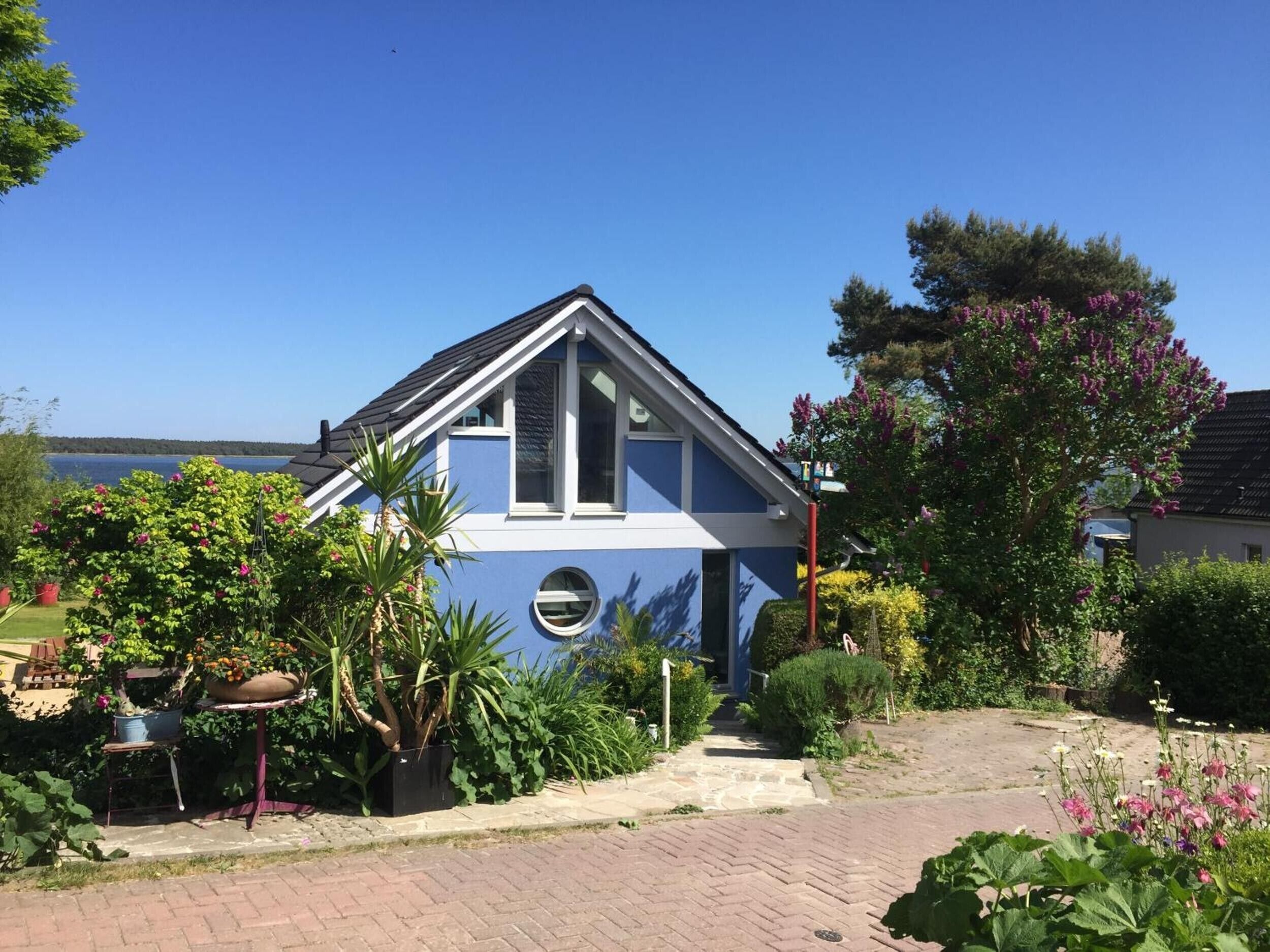 A blue house with a garden, a paved driveway, and a view of the water.