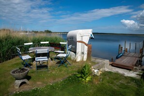 Un área de estar al aire libre frente al lago, con una mesa, sillas, una jardinera de piedra y un muelle de madera.