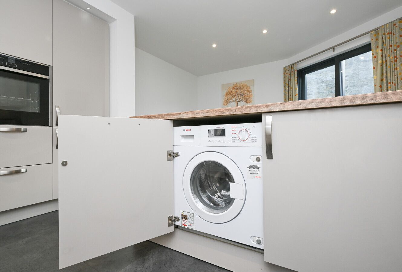A compact kitchen with a built-in washer and dryer, a microwave, and a window with curtains.