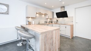 A modern kitchen with a central island, bar stools, and a flat-screen TV mounted above the island. - NEW to VRBO: Elegant Lerwick Townhouse • Harbour Views + Patio (Lerwick)