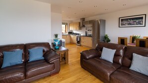 A modern living room with two brown leather sofas, a wooden coffee table, and a kitchen in the background.