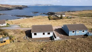 A coastal property with two main buildings, a gravel driveway, and a rocky shoreline.