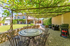 Eine Terrasse mit einem Mosaik-Tisch und -Stühlen, einem Grill und einer Pergola mit Kletterpflanzen.