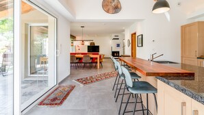 Une cuisine moderne dotée d’un long comptoir, de tabourets de bar et d’un coin repas avec une table et des chaises rouges.