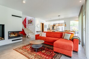 Un salon moderne avec une cheminée, un canapé rouge, un tapis à motifs et un escalier.