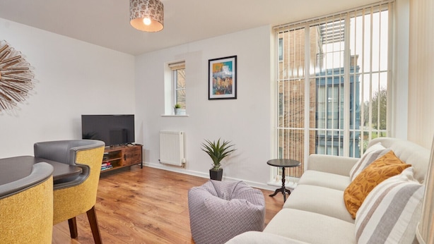 Un salon moderne avec un canapé, un fauteuil et un téléviseur posé sur un meuble en bois.