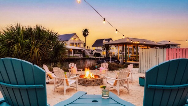 Une terrasse au bord de la plage, avec des fauteuils Adirondack, un foyer et des guirlandes lumineuses.