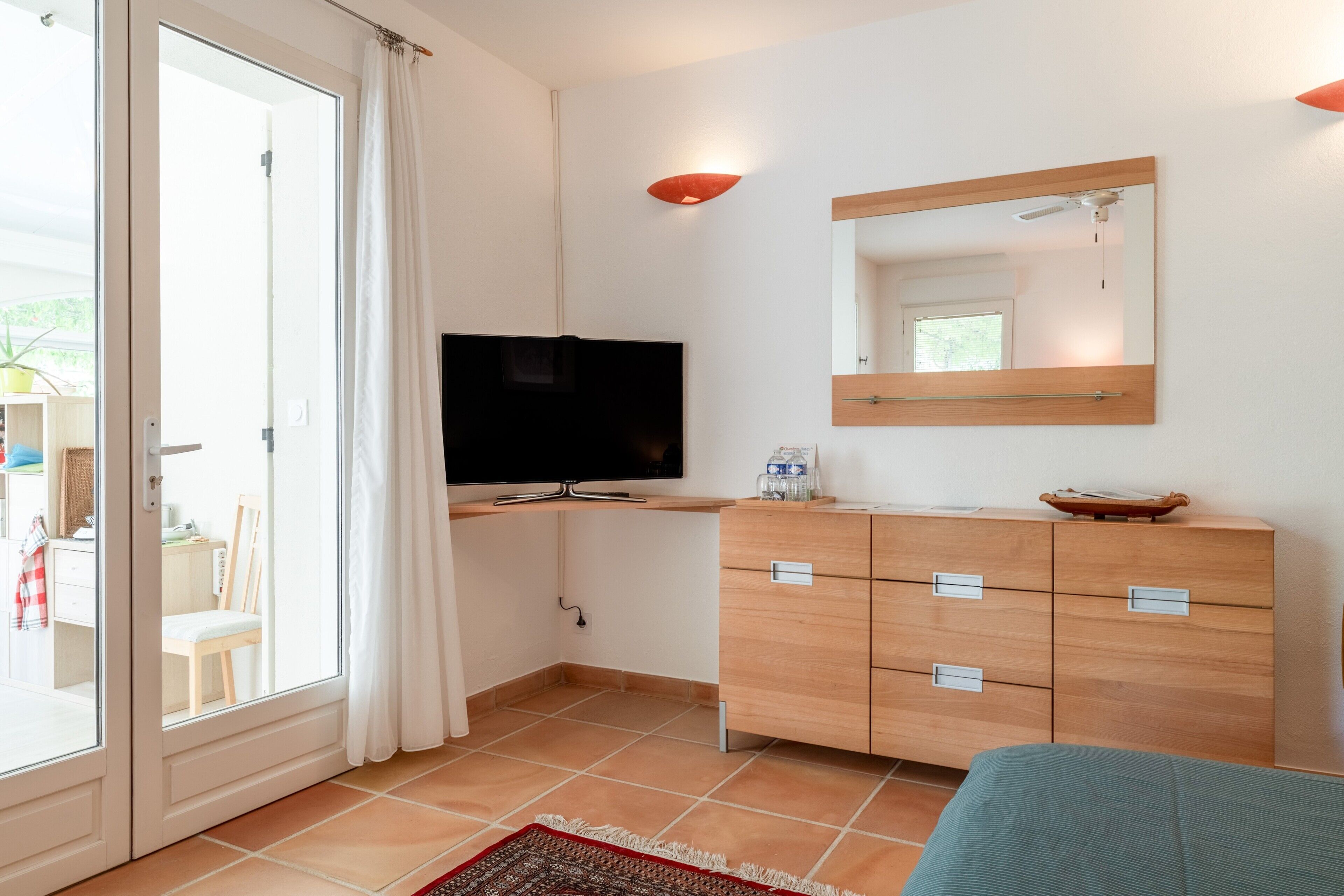 A room with a TV, wooden dresser, and a sliding glass door leading to an outdoor area.