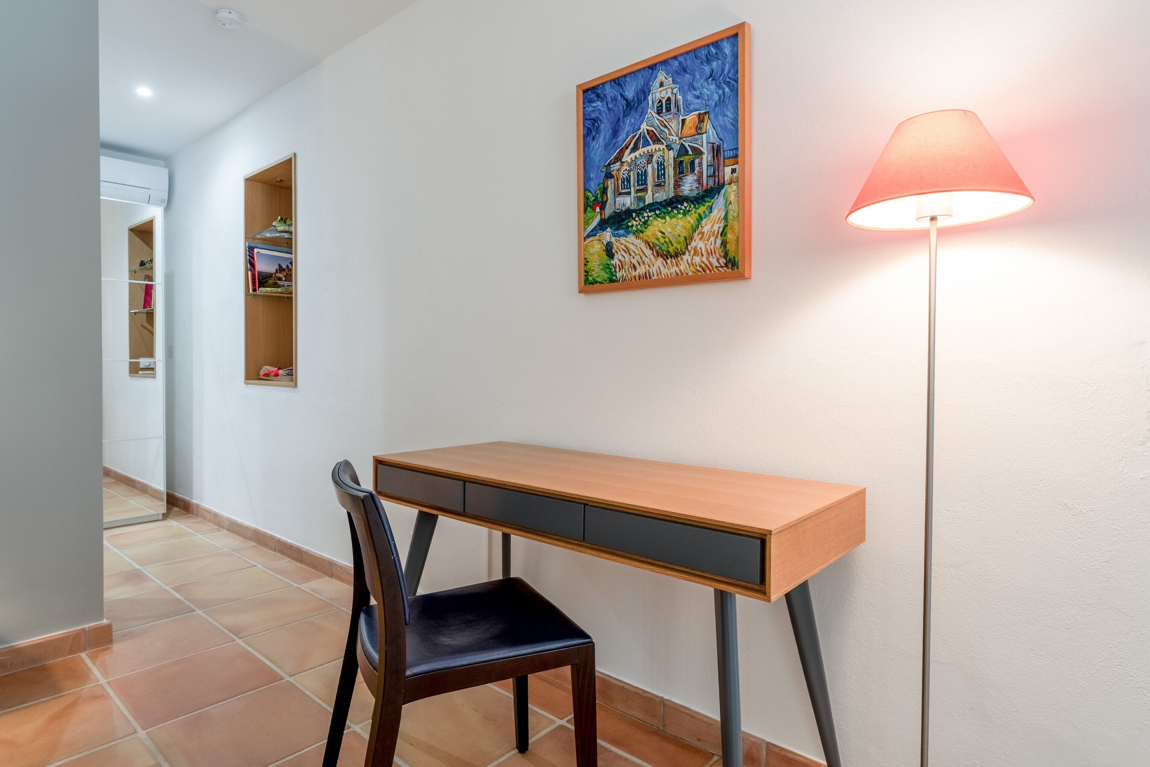 A study with a desk, chair, and lamp in a hallway.
