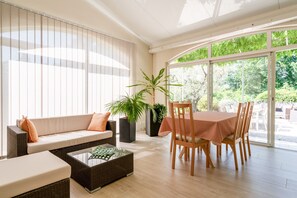 Ein sonnendurchflutetes Zimmer mit einer Couch, einem Esstisch, Stühlen, einem Couchtisch und einem großen Fenster.