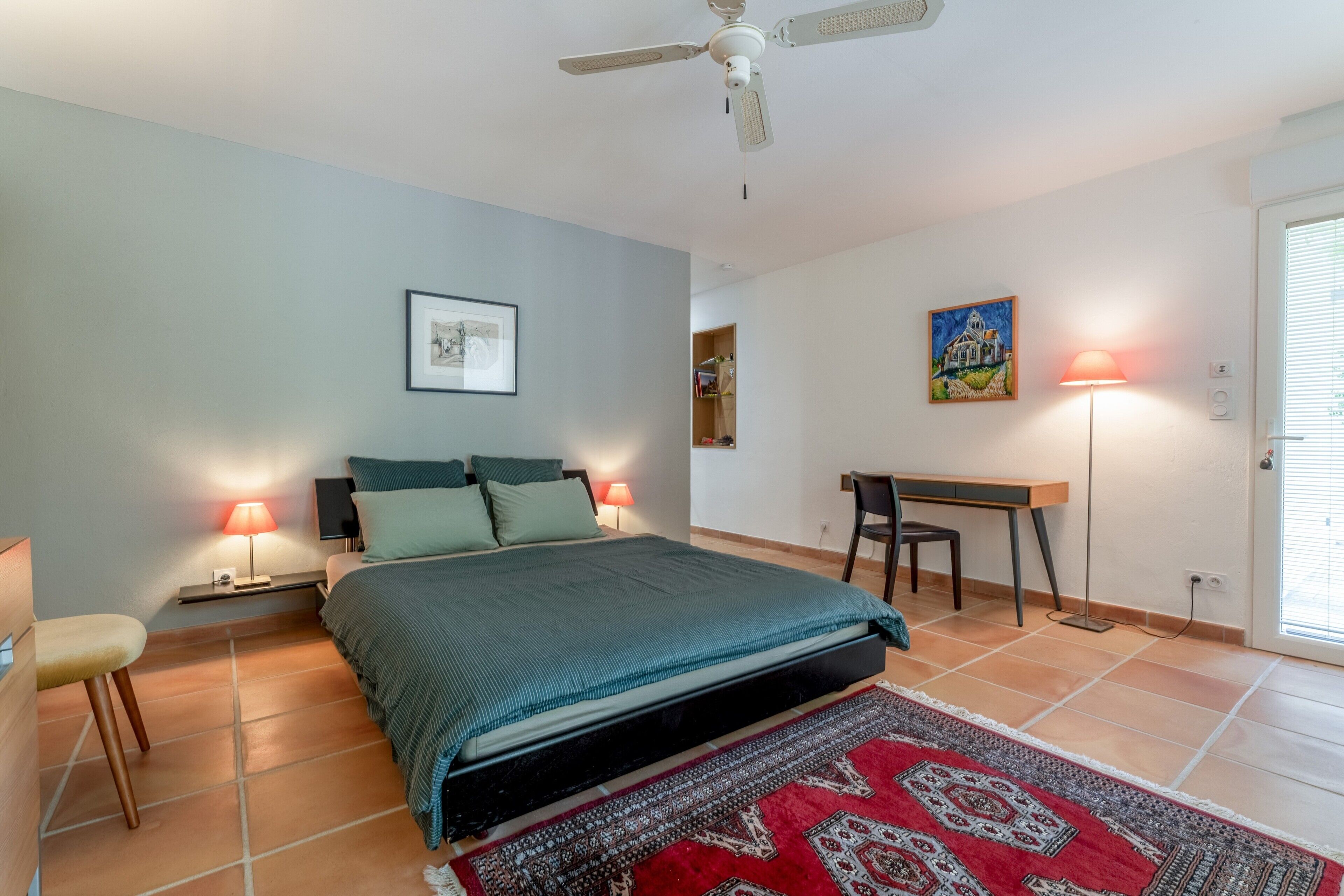 A bedroom with a bed, bedside lamps, a desk, and a chair.