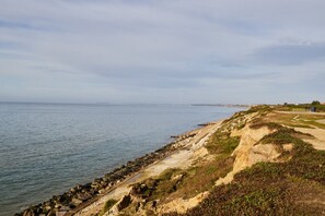 Eine Küstenlandschaft mit felsiger Küste, einem Sandweg und einem Blick auf das Meer in der Ferne.