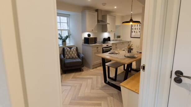 Une cuisine moderne avec des meubles blancs, un parquet en bois disposé en motif chevron, une table à manger et un canapé noir.