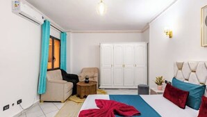 Ein Hotelzimmer mit Bett, Kleiderschrank, Sofa, kleinem Tisch und Zimmerpflanze.