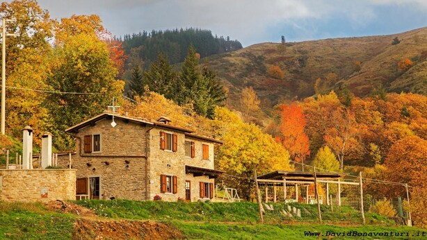 A stone house with a balcony, surrounded by autumn foliage and hills. - Room 'Camera B' – Prato Fiorito with Mountain View and Shared Pool (Bagni di Lucca)