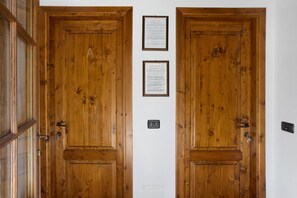 Twee houten deuren met een intercom en twee ingelijste aankondigingen op de muur.