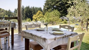 An outdoor dining area with a table set for four, surrounded by wooden chairs, a wooden pergola, and a view of a pool and trees. - Room 'Camera B' – Prato Fiorito with Mountain View and Shared Pool (Bagni di Lucca)