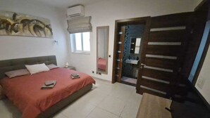A bedroom with a bed, bedside table, window, and an air conditioning unit. - Modern 3BR Apartment in Swieqi (Is-Swieqi)