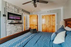 Un dormitorio con chimenea, puertas de madera, ventilador de techo y cama con ropa de cama azul.