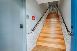 A wooden staircase with a stone accent wall, a blue door, and a fire alarm on the wall.