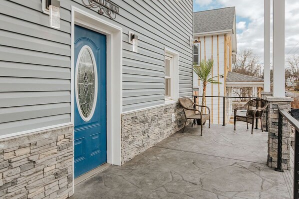 A house with a blue door, stone wall, and a patio with chairs.