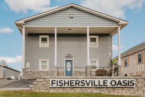 A building with a grey exterior, a blue door, and a sign reading "FISHERSVILLE OASIS" in front. - Valley Oasis: Luxury Fishersville Apartment (Fishersville)