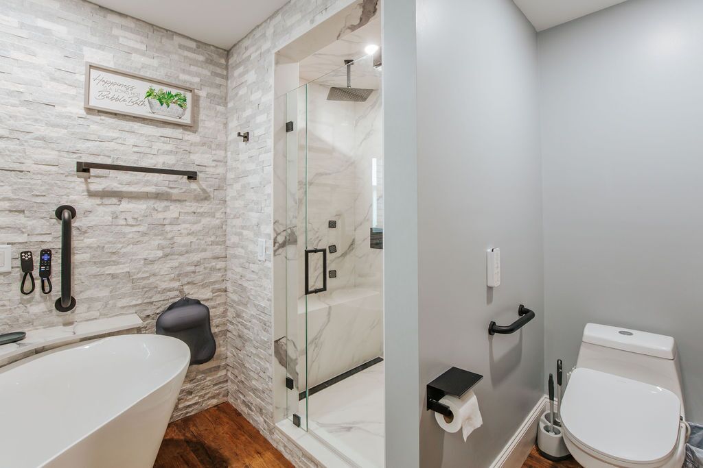 A bathroom with a stone wall, a glass-enclosed shower, a white toilet, and a bathtub.