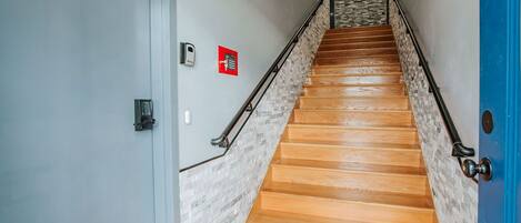 A wooden staircase with a stone accent wall, a blue door, and a fire alarm on the wall.