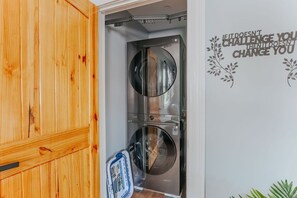 Une petite buanderie équipée de deux machines à laver en acier inoxydable, d’un meuble en bois et d’une citation inspirante sur le mur.