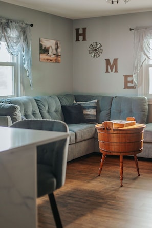 Ein gemütliches Wohnzimmer mit einem grauen Sofa, einem Holztisch und einer Wand, auf der das Wort „HOME“ mit Buchstaben geschrieben ist.