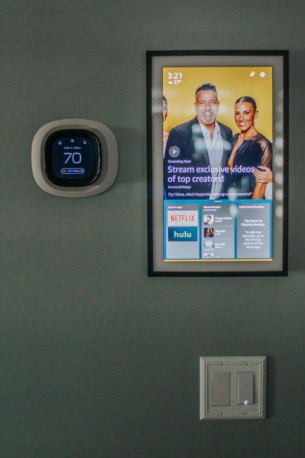 Termostato mostrando 21 grados Celsius, un anuncio enmarcado de servicios de transmisión y un interruptor de pared.