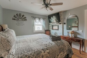 Ein Schlafzimmer mit einem großen Bett, einem Deckenventilator, einem Kamin, einem Schminktisch und einem Spiegel.