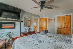 Ein Schlafzimmer mit Kamin, einem Bett mit gemustertem Überwurf, Deckenventilator und Holztüren.
