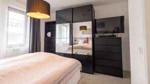 A modern bedroom with a bed, a TV, a wardrobe, and a window with curtains.