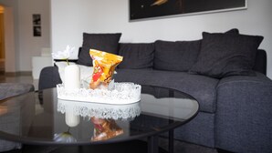 A modern living room with a glass coffee table, a white vase with a flower, and a snack packet.