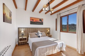 Une chambre avec un plafond en bois, un grand lit avec une tête de lit, des tables de chevet avec des lampes, une fenêtre avec des rideaux et un tableau au mur.